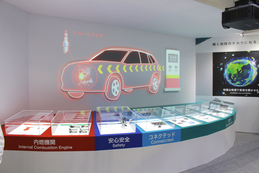 人とくるまのテクノロジー展2023（パシフィコ横浜）の日本特殊陶業ブース。「内燃機関」「安心安全」「コネクテッド」「次世代」の4分野の取り組みを展示。安心安全で扱う「アイアクセル」の体験を、隣の特設ブースで実施していた。